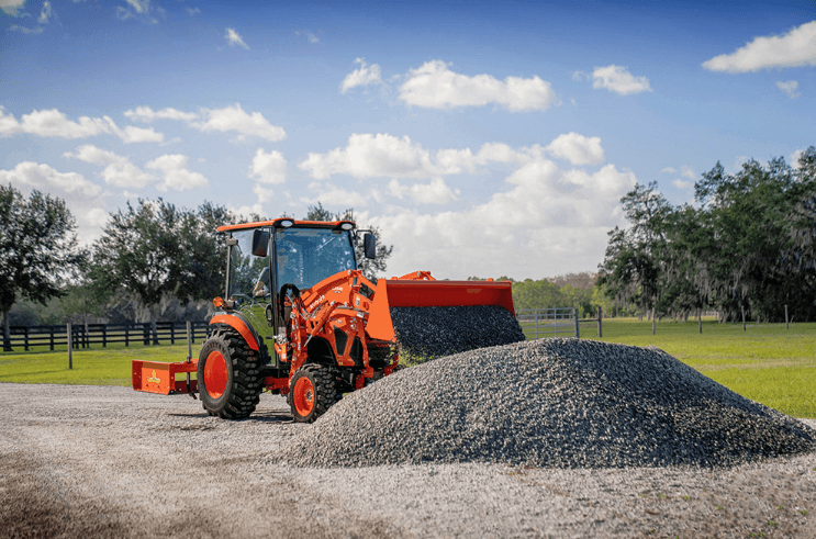 Man using Kubota compact tractor to move and dump gravel