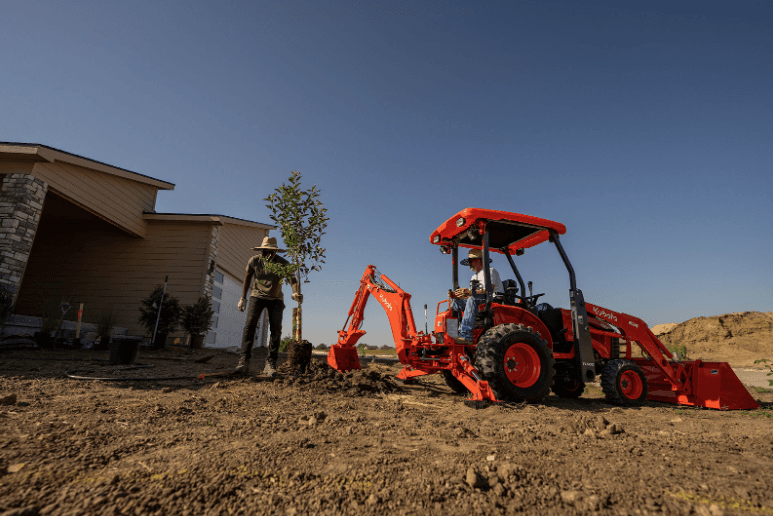 Landscapers using Kubota tractor loader backhoe to plant a tree