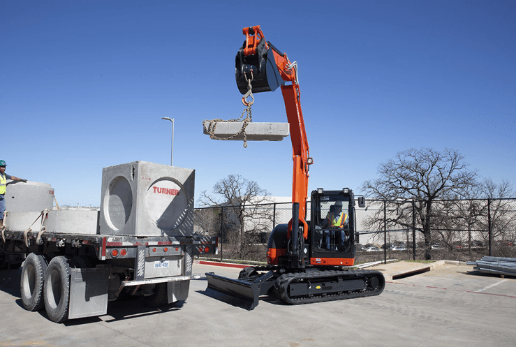 Kubota KX080-4 lifting large concrete blocks off the back of a trailer