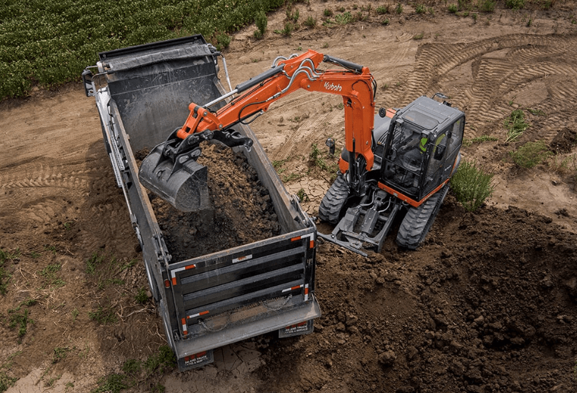 Kubota KX080-5 dumping dirt into the back of a dump truck