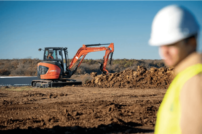 A compact excavator pictured with a construction worker