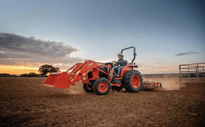 Man driving a tractor through a dirt fenced in area