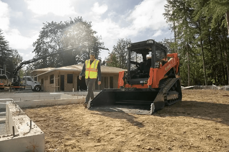 Man walking around the track loader on job site