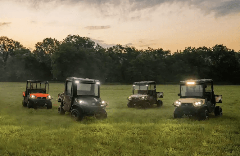 A lineup of Kubota Utility Vehicles outside with headlights on